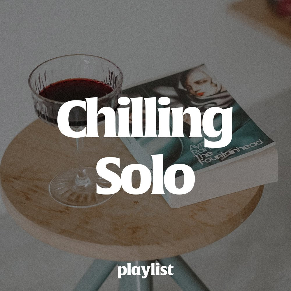 A glass of red wine sitting on a table next to a book. White text reads, "Chilling Solo" across the middle. 